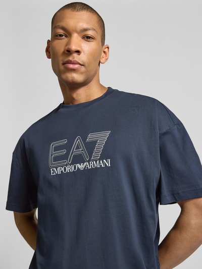Männermodel trägt T-Shirt mit Logo und Rundhalsausschnitt von EA7 Emporio Armani aus reiner Baumwolle, Regular-Fit, Nahaufnahme Oberkörper.
