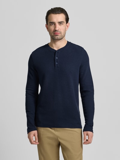 Męski model nosi Regular Fit Longsleeve mit Knopfleiste od MCNEAL z elastycznej bawełny, okrągły dekolt, faktura, krój regular fit, granatowy, widok całej sylwetki z przodu.