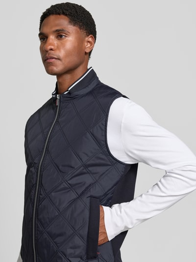 Männermodel trägt Regular Fit Weste in Stepp-Optik von Christian Berg Men, dunkelblau, Stehkragen, Reißverschluss, Ganzkörperansicht von vorne.