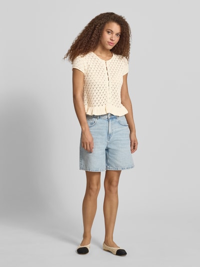 Frauenmodel trägt Stricktop mit Knopfverschluss und Schößchendetail von Review aus Reine Baumwolle im Regular-Fit, helles Creme, Rückenlänge 51 cm in Größe S, kombiniert mit hellblauer Jeansshorts, Ganzkörperansicht von vorne.
