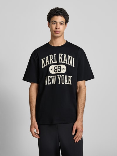 Männermodel trägt Oversized Fit T-Shirt mit Logo-Print Modell 'Heritage' von KARL KANI in Schwarz aus Reine Baumwolle, Rundhalsausschnitt, Rückenlänge bei Größe M 71 cm, Herren T-Shirt, Ganzkörperansicht von vorne.