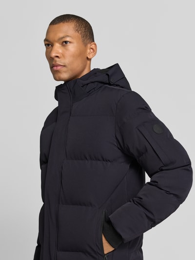 Männermodel trägt schwarze Regular Fit Steppjacke mit Kapuze und verdecktem Reißverschluss von Cars Jeans, Nahaufnahme Oberkörper. Modell 'JAXHAM', Material-Mix mit Stretch, Reißverschlusstaschen, neutrale glatte Textur.