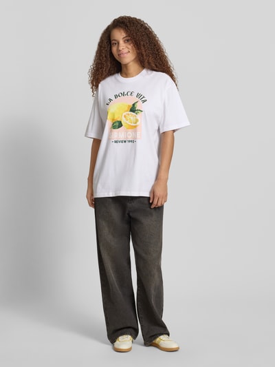 Frauenmodel trägt T-Shirt mit rückseitigem Motiv-Print von REVIEW in Weiß, Oversized-Schnitt aus Reine Baumwolle, Rundhalsausschnitt, Ganzkörperansicht von vorne.