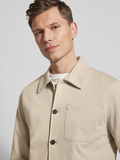 Männermodel trägt Relaxed Fit Hemdjacke mit Brusttasche von Lindbergh in Beige, glatte Struktur, Umlegekragen, Nahaufnahme Oberkörper.