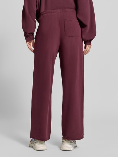 Frauenmodel trägt Straight Fit Sweatpants aus elastischem Baumwoll-Mix von American Vintage in Dunkelrot, Modell 'ATUBAY', Ganzkörperansicht Rückansicht.