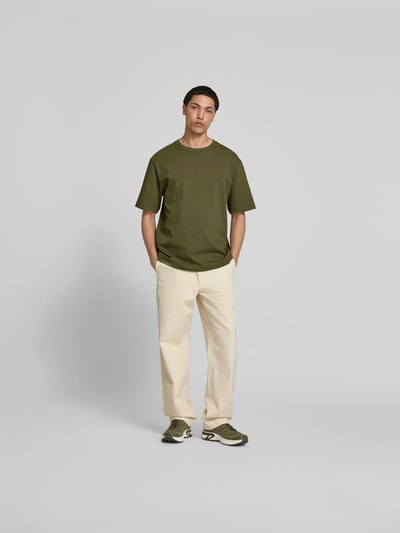 Männermodel trägt T-Shirt mit Rundhalsausschnitt von Filippa K in Olivgrün, reine Baumwolle, Relaxed Fit, Ganzkörperansicht von vorne.