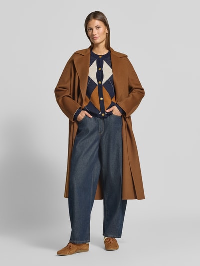 Frauenmodel trägt Regular Fit Strickjacke aus reiner Wolle von GANT in Dunkelblau mit Rauten, dazu brauner Mantel, Jeans, Ganzkörperansicht von vorne. Damen Strickjacke von GANT.