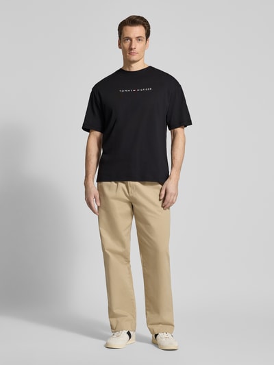 Männermodel trägt Regular Fit T-Shirt aus reiner Baumwolle von Tommy Hilfiger in Schwarz, unifarben, mit Label Print, Ganzkörperansicht von vorne.