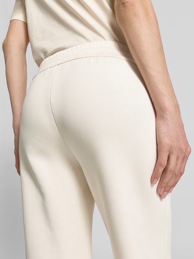 Frauenmodel trägt Sweatpants mit elastischem Bund und Logo-Print von ARMANI EXCHANGE in Creme, glatte Textur, seitliche Eingrifftaschen, Ganzkörperansicht Rückansicht, Damen Straight Fit, Innenbeinlänge bei Größe S: 72 cm.