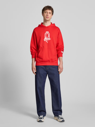 Männermodel trägt Relaxed Fit Hoodie mit Känguru-Tasche von PUMA PERFORMANCE in Rot aus Reine Baumwolle mit Label-Detail, Ganzkörperansicht von vorne.