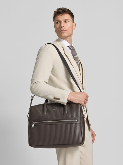 Männermodel trägt Laptoptasche aus echtem Rindsleder Modell 'DAXTER' von BOSS, unifarben, rechteckig, genarbtes Leder, Ganzkörperansicht von vorne.