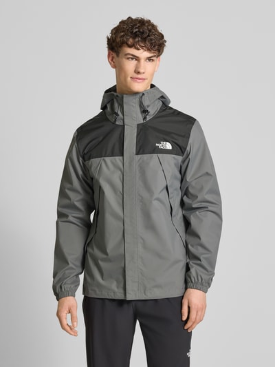 Męski model nosi Regular Fit Jacke mit Logo-Print Modell 'Antora' od The North Face w odcieniach szarości, z kapturem i kieszeniami, krój regular fit, długość tyłu w rozmiarze M: 74 cm, szerokość w ramionach w rozmiarze M: 47 cm, szerokość w klatce piersiowej w rozmiarze M: 58 cm, długość rękawa w rozmiarze M: 68 cm, widok całej sylwetki z przodu.