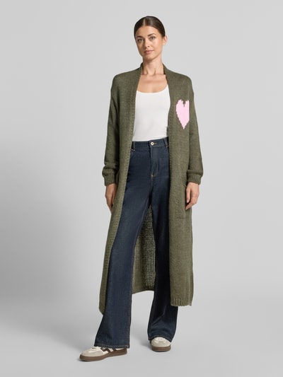 Frauenmodel trägt Strickjacke mit Woll-Anteil von miss goodlife in Oliv mit rosa Herz-Motiv, lockere Passform, Ganzkörperansicht von vorne.