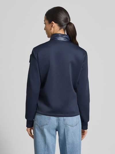 Frauenmodel trägt Steppjacke mit Label-Patches Modell 'HASKEL' von Blauer Usa in Dunkelblau, glatte Struktur, ganzkörperansicht Rückansicht. Kontext: gerader Schnitt, Stehkragen, Zweiwege-Reißverschluss, seitliche Reißverschlusstaschen, Maße bei Gr. S: Rückenlänge 57 cm, Schulterbreite 36 cm, Brustweite 49 cm, Ärmellänge 63 cm.