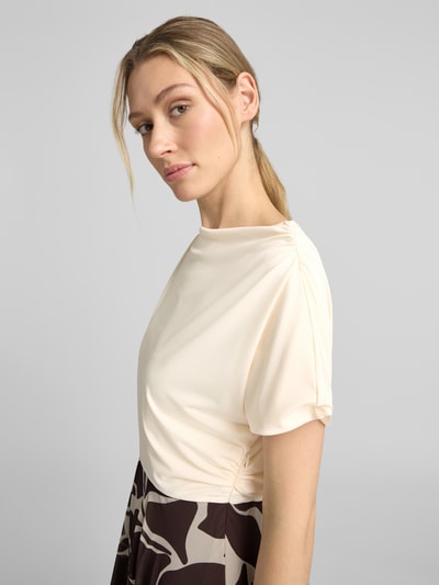 Frauenmodel trägt Cocktailkleid im 2-in-1-Look mit Drapierungen von Christian Berg Cocktail in A-Linie und Midikleid, Nahaufnahme Oberkörper. Rückenlänge bei Größe 36: 116 cm, Brustweite bei Größe 36: 45 cm. Helle, glatte Stoffstruktur oben, abstraktes Muster unten.