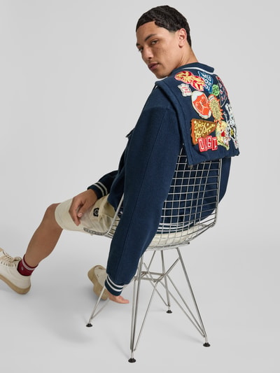 Männermodel trägt Relaxed Fit Jacke mit Motiv-Patches von Kenzo in Dunkelblau, Baumwolle, bunte Applikationen, Rückansicht, Nahaufnahme Oberkörper.