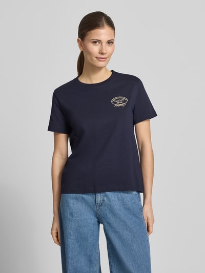 Frauenmodel trägt T-Shirt mit Rundhalsausschnitt und Logo von Gant in Dunkelblau, reine Baumwolle, Regular Fit, Nahaufnahme Oberkörper.