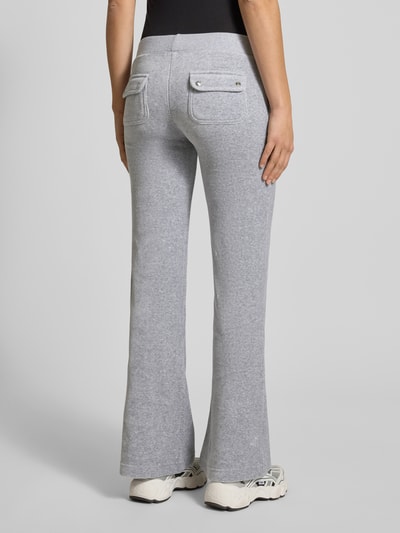 Frauenmodel trägt Low Rise Sweatpants mit elastischem Bund Modell 'LAYLA' von Juicy Couture aus grauem Baumwoll-Mix mit Stretch-Anteil, Flared-Cut, Eingrifftaschen und 39 cm Innenbeinlänge bei Größe S, Ganzkörperansicht Rückansicht.