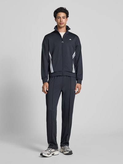 Męski model nosi Straight Fit Sweatpants mit Logo-Detail model 'Latucci' od Ellesse, elastyczna mieszanka materiałów, krój straight fit, detal z logo, elastyczny pas, ozdobne szwy, długość wewnętrzna nogawki w rozmiarze M: 79 cm, widok całej sylwetki z przodu.