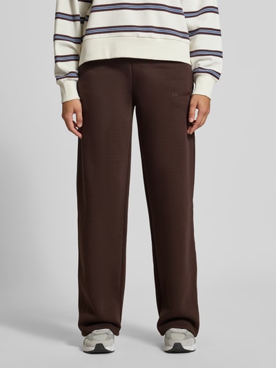 Frauenmodel trägt Sweathose mit geradem Bein von REVIEW in Dunkelbraun, Baumwoll-Mix, elastischer Bund, Logo-Print, Ganzkörperansicht von vorne.