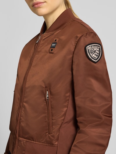 Frauenmodel trägt Bomberjacke mit Reißverschlusstaschen Modell 'LAURIE' von Blauer Usa in Braun, glänzende Optik, Label-Patches, Nahaufnahme Oberkörper.