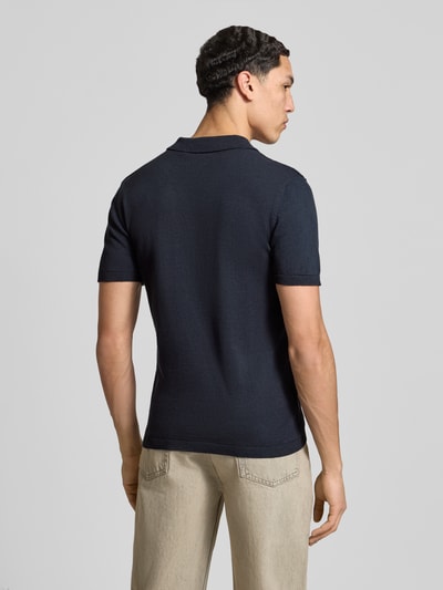 Männermodel trägt Slim Fit Poloshirt in Strick-Optik Modell 'Baron' von Blend aus reiner bawełna, kołnierzyk polo, krój slim fit, długość tyłu w rozmiarze M: 65 cm, ciemnoniebieski materiał, imitacja dzianiny, Ganzkörperansicht Rückansicht.