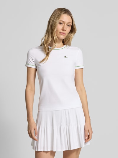 Frauenmodel trägt Slim Fit T-Shirt aus Baumwoll-Mix von Lacoste, unifarben weiß mit Logo-Stitching und Kontrastpaspel, Ganzkörperansicht von vorne.
