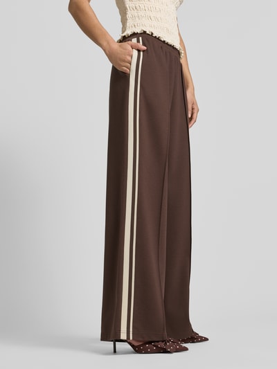 Frauenmodel trägt Jog Pants mit französischen Eingrifftaschen von Jake*s Casual in Braun mit cremefarbenen Seitenstreifen, Wide Leg Fit, Material-Mix mit Stretch-Anteil, elastischer Bund, Ganzkörperansicht von vorne.