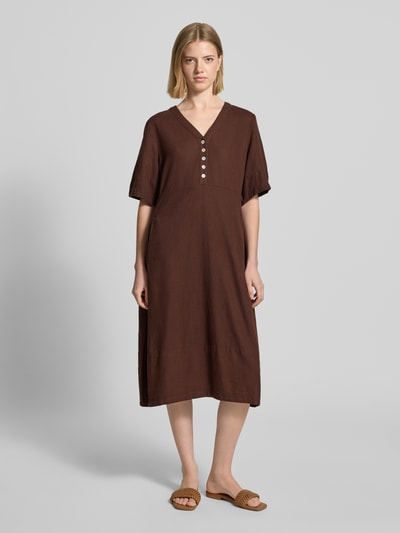 Frauenmodel trägt knielanges Kleid aus Leinen-Viskose-Mix Modell 'Lava' von FREE/QUENT in Braun, A-Linie, V-Ausschnitt, Knopfleiste, Ganzkörperansicht von vorne. Rückenlänge 96 cm, Brustweite 43 cm, Ärmellänge 29 cm.