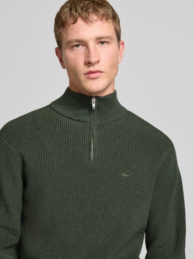 Männermodel trägt Strickpullover mit Stehkragen von Levi's®, dunkelgrün, reine Baumwolle, gerippt, kurzer Reißverschluss, Nahaufnahme Oberkörper.