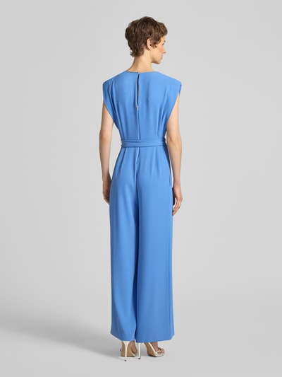 Modelka prezentuje niebieski kombinezon z dekoltem w serek i wiązanym paskiem, mieszanka materiałów z dodatkiem streczu, krój regular fit, Jumpsuit mit V-Ausschnitt und Bindegürtel von comma, długość tyłu w rozmiarze 36: 41 cm, szerokość w rozmiarze 36: 38 cm, całkowita długość w rozmiarze 36: 145 cm, długość wewnętrzna nogawki w rozmiarze 36: 73 cm, widok całej sylwetki z tyłu.