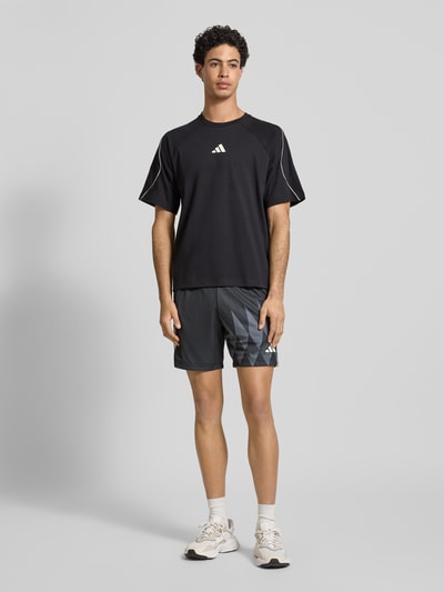 Männermodel trägt T-Shirt mit Label-Print von adidas Sportswear, schwarze Farbe, Reine Baumwolle, Regular-Fit, Ganzkörperansicht von vorne.