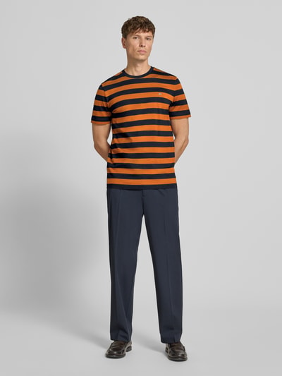 Männermodel trägt Regular Fit T-Shirt mit Logo-Stitching von Christian Berg Men, orange-schwarz gestreift, Reine Baumwolle, Ganzkörperansicht von vorne.
