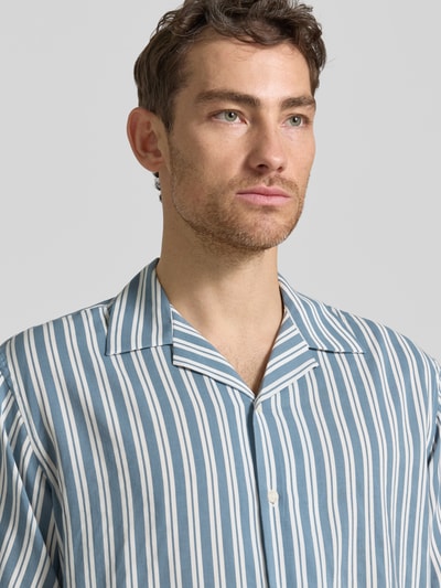 Männermodel trägt Relaxed Fit Freizeithemd aus Bio-Baumwoll-Modal-Mix Modell 'RELAXAIR' von SELECTED HOMME, Optik: Unifarben mit blauen Streifen, Reverskragen, durchgehende Knopfleiste, Ärmelform: Kurzarm, Nahaufnahme Oberkörper.