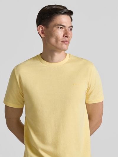Männermodel trägt T-Shirt mit Rundhalsausschnitt und Label-Stitching von Gant, reine Baumwolle, Regular Fit, hellgelb, Ganzkörperansicht von vorne.