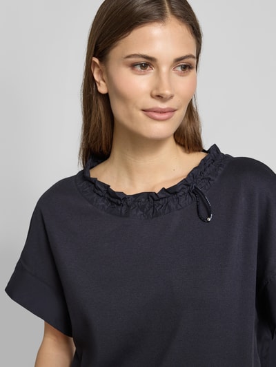 Kobiece modelka nosi T-Shirt mit Eingrifftasche am Saum von Marc Cain, mieszanka bawełny i elastanu, luźny krój, okrągły dekolt z tunelem, wpuszczana kieszeń, długość tyłu 51 cm w rozmiarze 36, zbliżenie na górną część ciała.