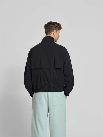 Männermodel trägt Blouson mit Stretch-Anteil von Forét in Schwarz, lockere Passform, elastische Abschlüsse, Ganzkörperansicht Rückansicht.