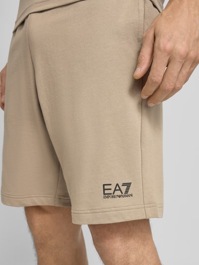 Mężczyzna nosi Szorty z elastycznym pasem i logo od Armani EA7 Emporio Armani, bawełna, krój regular fit, beżowy, detal, zbliżenie na nogi.