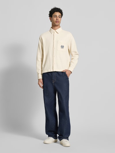 Männermodel trägt Regular Fit Freizeithemd mit Logo-Stitching von REVIEW in Creme mit Strukturmuster, kombiniert mit blauer Hose, Ganzkörperansicht von vorne.