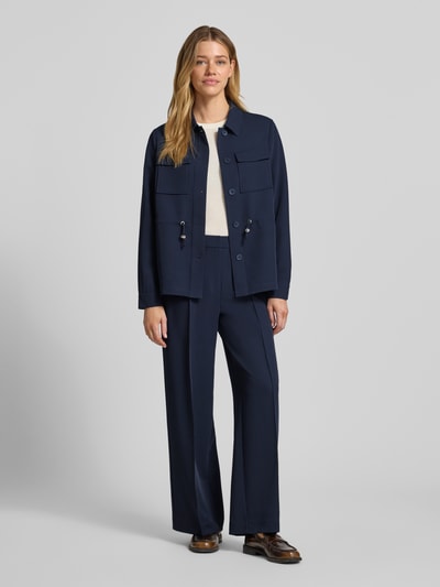 Modelka nosi Regular Fit Longblazer mit Brustpattentaschen von s.Oliver BLACK LABEL, ciemnogranatowy, gładki materiał, długi fason, tunel w talii, zapięcie na jeden rząd guzików, długie rękawy z mankietami, kieszenie z patkami na piersi, widok całej sylwetki z przodu.