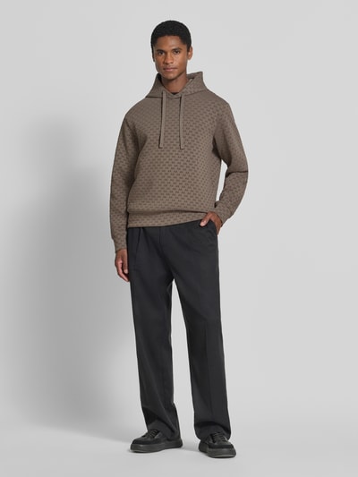 Männermodel trägt Regular Fit Hoodie aus Baumwoll-Mix von Armani Exchange mit Allover-Logo-Print in Braun, Ganzkörperansicht von vorne. Rückenlänge bei Größe M: 66 cm, Ärmellänge bei Größe M: 63 cm, Elastischer Baumwoll-Mix, Kapuze mit Tunnelzug, elastische Abschlüsse.