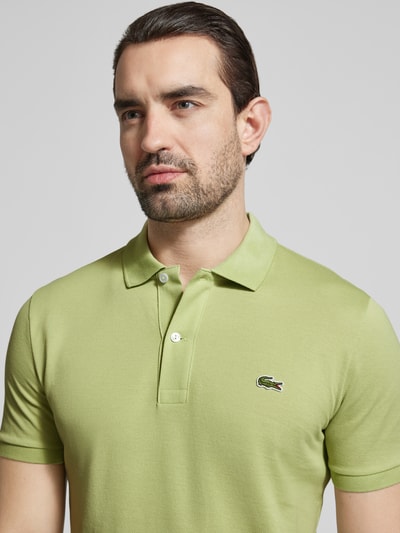 Männermodel trägt Slim Fit Poloshirt aus reiner Baumwolle von Lacoste in Hellgrün, unifarben, Logo-Stitching, Nahaufnahme Oberkörper.
