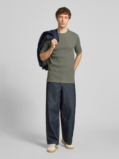 Männermodel trägt Regular Fit T-Shirt aus Baumwoll-Mix Modell 'TOBIE' von Only & Sons in Khaki mit Waffel-Struktur, unifarben, Ganzkörperansicht von vorne.