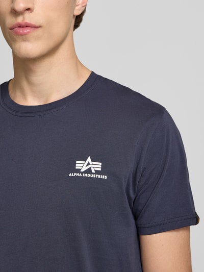 Männermodel trägt T-Shirt mit Logo und Rundhalsausschnitt von Alpha Industries, Reine Baumwolle, Regular-Fit, Nahaufnahme Oberkörper.