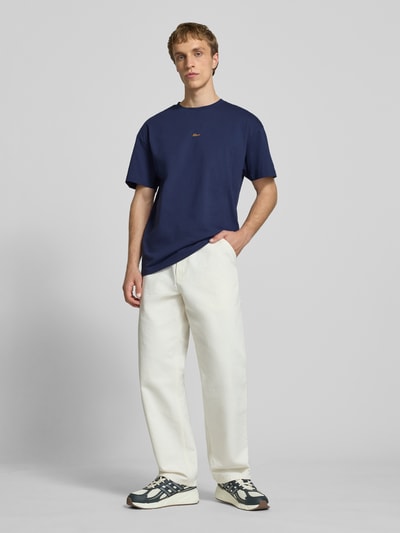 Mannelijk model draagt Regular Fit T-Shirt met Logo-Stitching van BLKVIS, zuiver katoen, regular fit, ronde hals, lengte achterkant maat M 62 cm, blauw, witte broek, sneakers, volledig lichaamsaanzicht van voren.