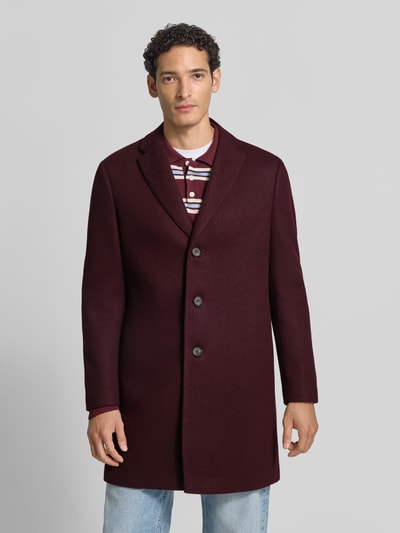 Männermodel trägt Relaxed Fit Mantel aus reiner Baumwolle von MCNEAL in Bordeaux, glatte Oberfläche, Reverskragen, Ganzkörperansicht von vorne.