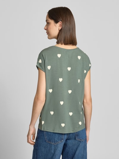 Frauenmodel trägt Relaxed Fit T-Shirt aus Lyocell-Mix Modell 'AVA' von Vero Moda mit Allover-Herz-Print, kurzarm, grün, Ganzkörperansicht Rückansicht.