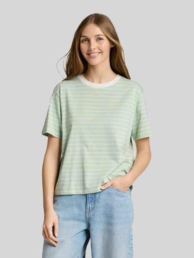 Frauenmodel trägt Relaxed Fit T-Shirt aus reiner Baumwolle von Tom Tailor Denim mit Optik:Allover-Muster, gestreift, Logo-Patch, Rundhals, Kurzarm, Materialverarbeitung: Jersey, Farbe in Pastellgrün und Weiß, Ganzkörperansicht von vorne.