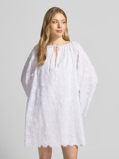 Frauenmodel trägt Minikleid mit Spitze und Kimonoärmel von MICHAEL Michael Kors aus Reine Baumwolle, Loose-Fit, Serafino-Ausschnitt mit Schnürung, blickdichtes Unterkleid, Farbe Weiß, florale Struktur, Ganzkörperansicht von vorne.