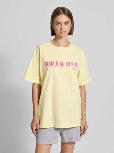 Frauenmodel trägt T-Shirt mit Rundhalsausschnitt Modell 'AM to PM' von OH APRIL, gelb mit rosa Print, Oversized, reine Baumwolle, Ganzkörperansicht von vorne.